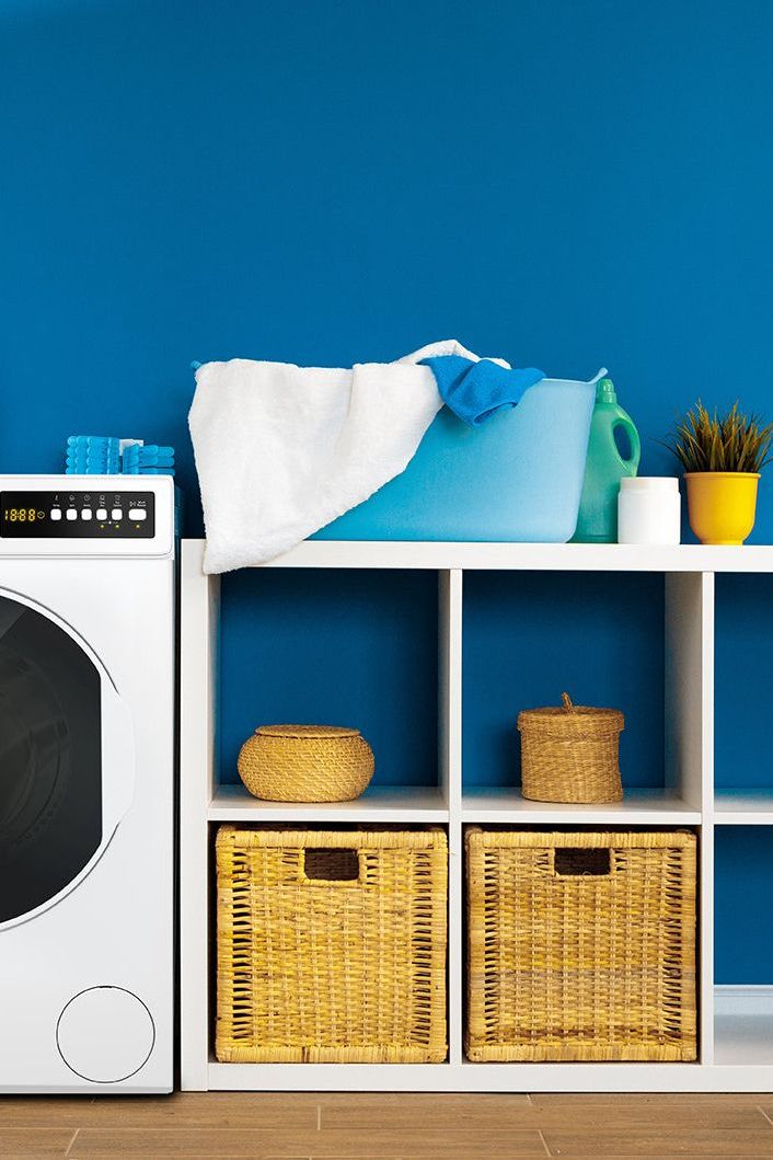 Laundry room with washing machine, shelves, and cleaning supplies against a blue wall.