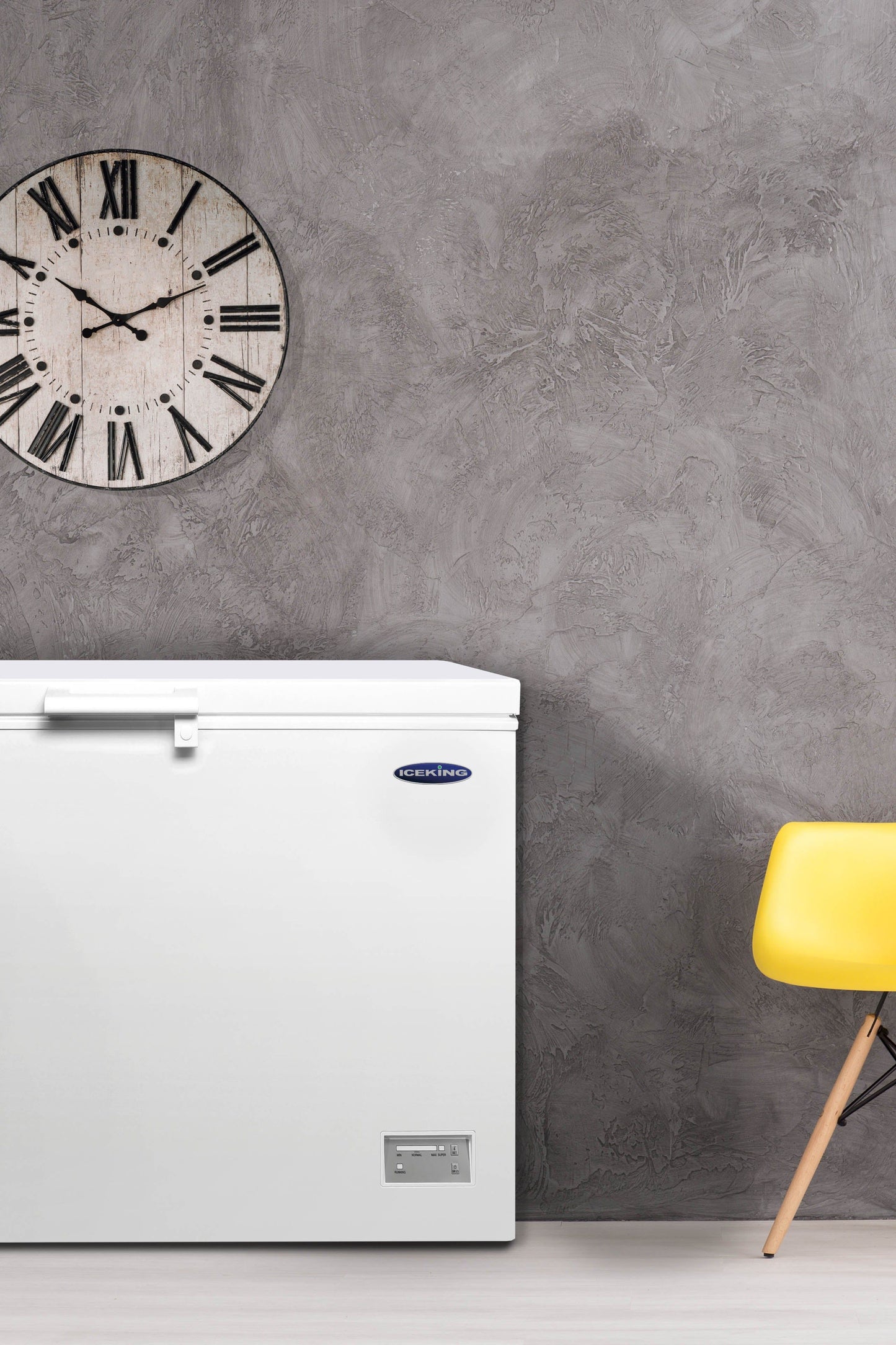 White freezer against a gray wall with a yellow chair and clock.